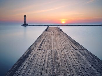 Pier and lighthouse over lake against sky during sunrise