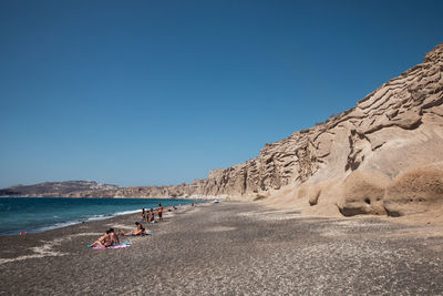 People on beach against clear blue sky