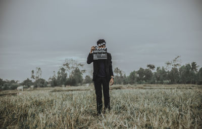 Full length of young man holding film slate on field