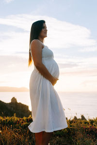 Pregnant woman standing on field by sea against sky