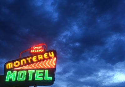 Low angle view of illuminated sign against sky at night