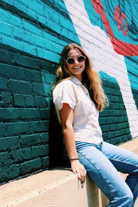 Woman wearing sunglasses against wall