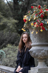 Beautiful young woman sitting by sculpture at park