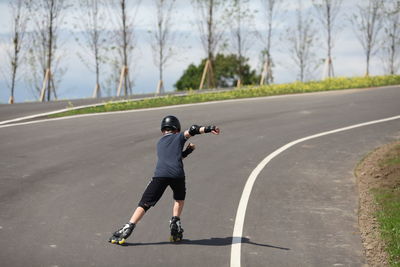 Rear view of man skateboarding on road