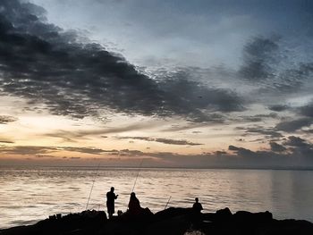 Silhouette people on beach against sky during sunset