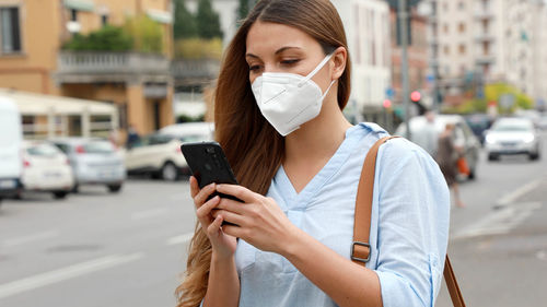 Woman wearing mask using mobile phone while standing on street