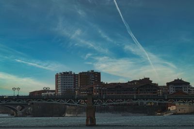 Bridge over river by buildings in city against sky