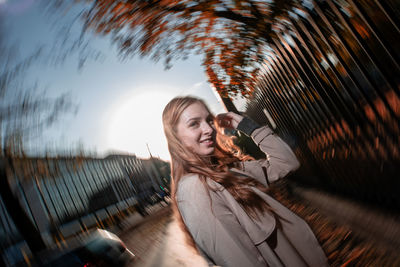 Portrait of smiling young woman with arms raised against sky