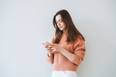 Portrait of woman in casual knitted sweater using mobile phone in hand on the grey background