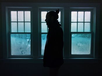 Side view of man standing by glass window during winter