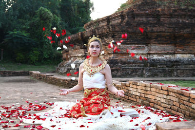 Woman in traditional clothing throwing petals against old ruin