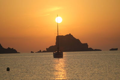 Silhouette sailboats in sea against orange sky