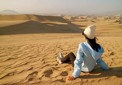 Woman sitting on sand dune in desert