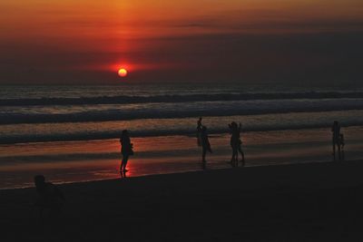 Silhouette people on beach against sky during sunset