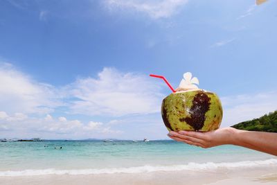 View of hand holding coconut drink on beach