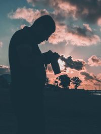 Silhouette man with camera standing against cloudy sky during sunset