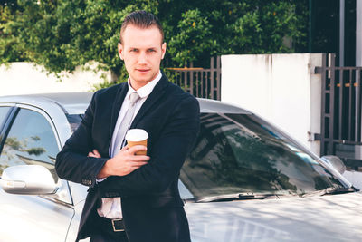 Portrait of businessman standing with car on road