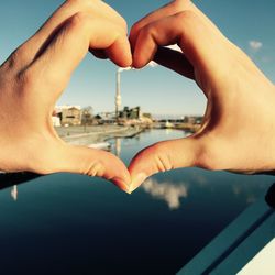 Cropped image of woman making heart shape by river against sky