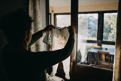 Rear view of woman holding glass window at home