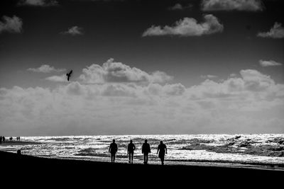Silhouette people standing at beach against cloudy sky