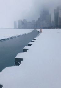 Frozen river by buildings against sky in city during winter