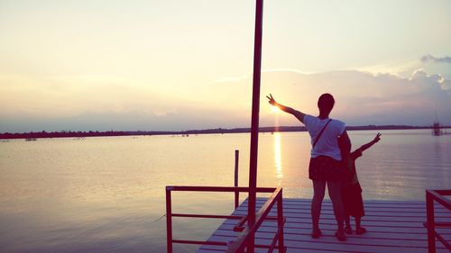 Rear view of man standing by railing against sea during sunset