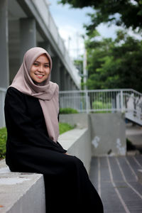 Portrait of smiling young woman standing against built structure