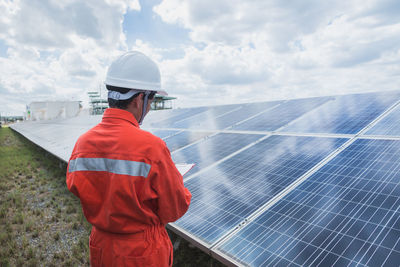 Engineer standing amidst solar panel against cloudy sky