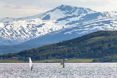 People windsurfing on sea against snowcapped mountains