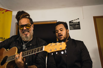 Adult bearded men in black clothes playing guitar and singing song in light studio