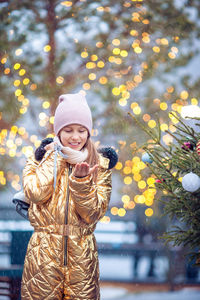 Portrait of smiling young woman standing against christmas tree