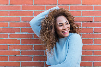 Happy mixed race woman with white perfect smile, long curly hair, glamour makeup and blue jumper 