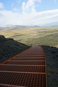 High angle view of steps over mountain by grassy field against cloudy sky