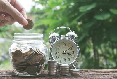 Cropped hand putting coin in jar against trees