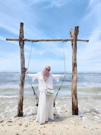 Rear view of woman standing at beach against sky