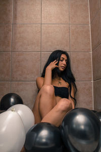 Beautiful young woman sitting amidst balloons in bathroom
