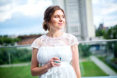 Beautiful woman holding drink looking away while standing outdoors