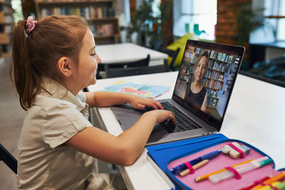 Student litttle girl having video class remotely with her teacher on laptop sitting at desk