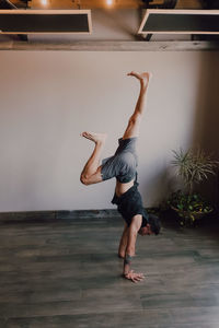 Back view of faceless barefooted man in sportswear standing upside down in downward facing dog pose while training in contemporary gym