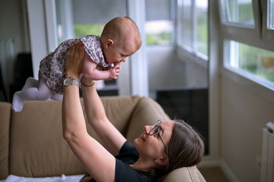 Mother sitting on a sofa and playing with cute little baby girl