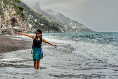 Full length of young woman standing at beach against clear sky