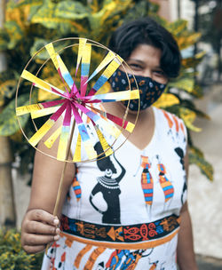 Portrait of a beautiful indian girl in ethnic casual and protective face mask, holding a pinwheel. 