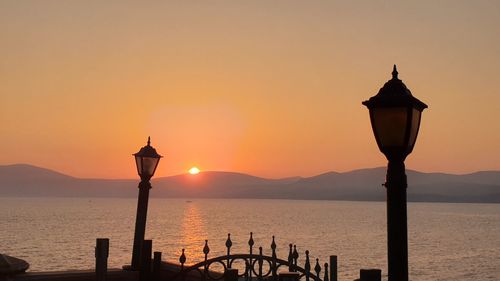 Silhouette street light by sea against sky during sunset