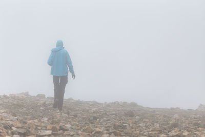 Rear view of person walking on rocky field during foggy weather