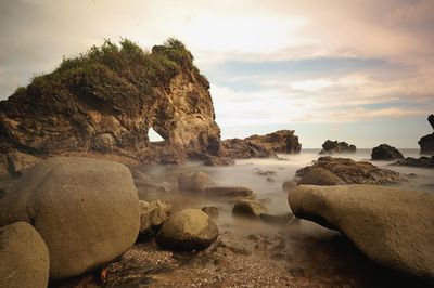 Rock formation on beach against sky during sunset