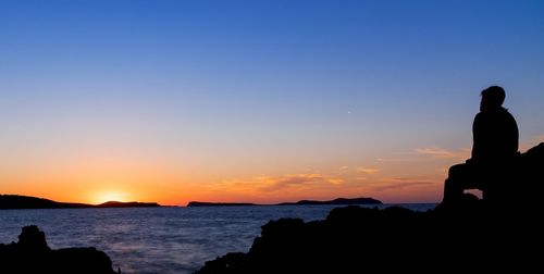 Silhouette people looking at sea against sky during sunset