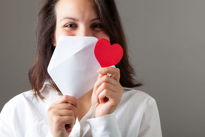 Portrait of young woman holding heart shape against white background