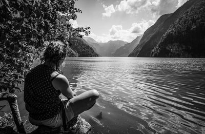 Woman sitting by lake against sky