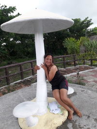 Portrait of smiling young woman standing by sculpture against sky