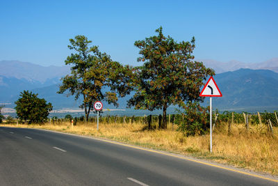 Road sign by trees against clear sky